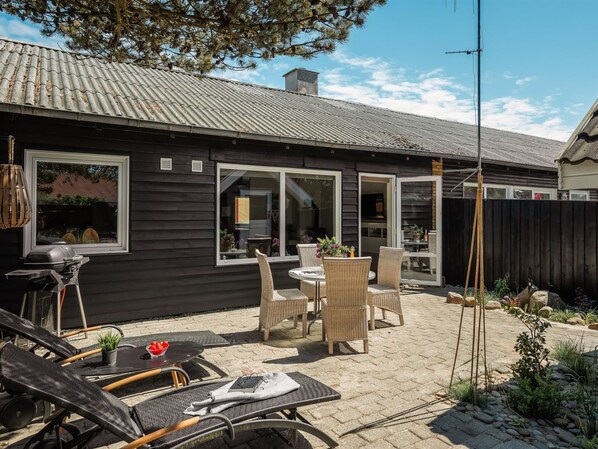 Een huis met een patio, meubilair buiten, een barbecue en uitzicht op de achtertuin.