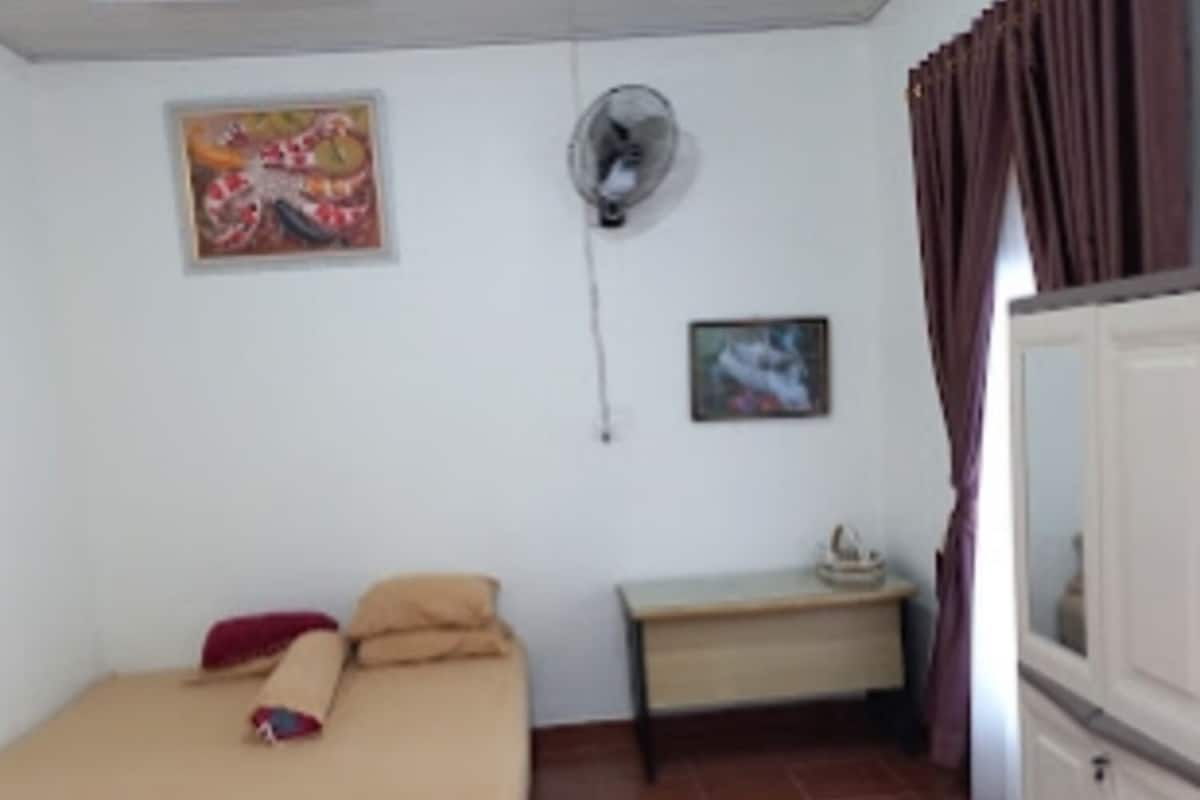 Una habitación con cama, escritorio, ventilador y armario.