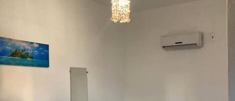 Habitación de hotel con cama, mesita de noche con arreglo floral, lámpara colgante, un cuadro en la pared y un equipo de aire acondicionado.