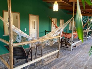 A hammock setup with wooden frames and a woven hammock, wooden benches, and a green wall with doors. - Pousada Kalango (Cajueiro da Praia)