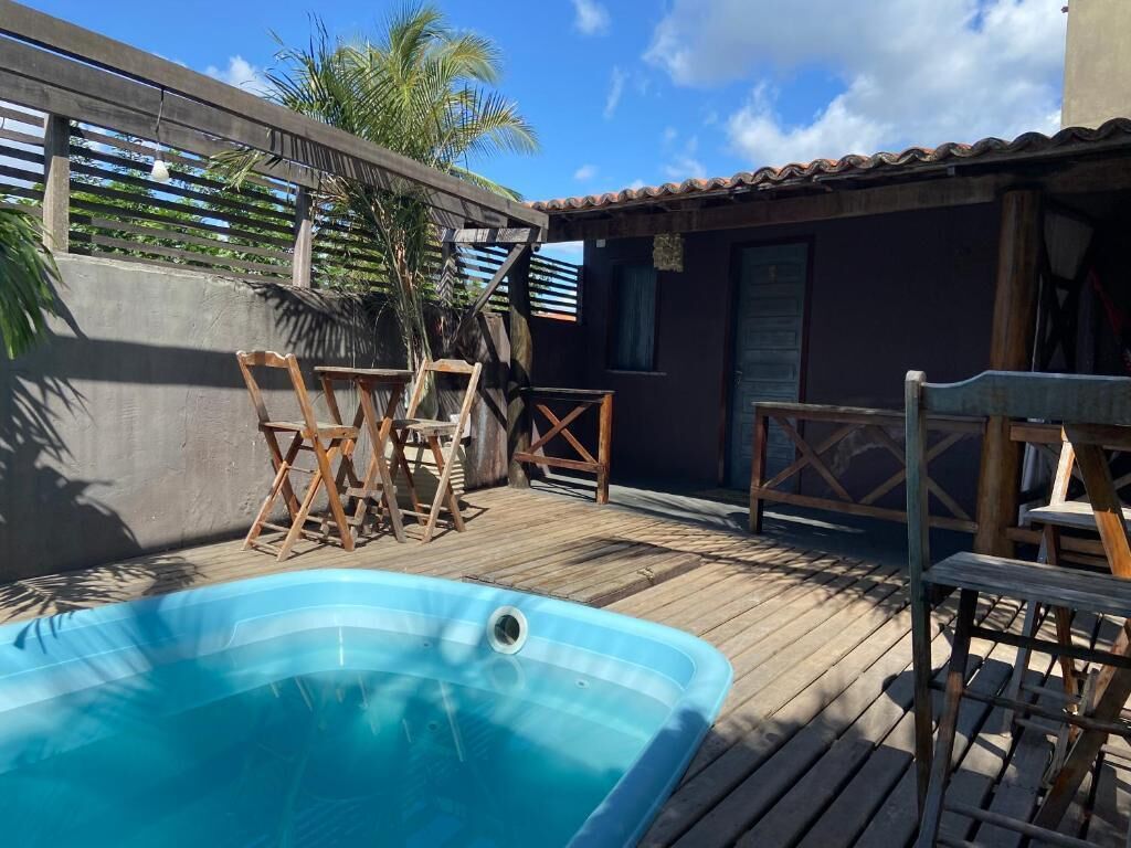 Um deck de madeira com piscina, cadeiras de madeira e um pequeno edifício com telhado de azulejos.