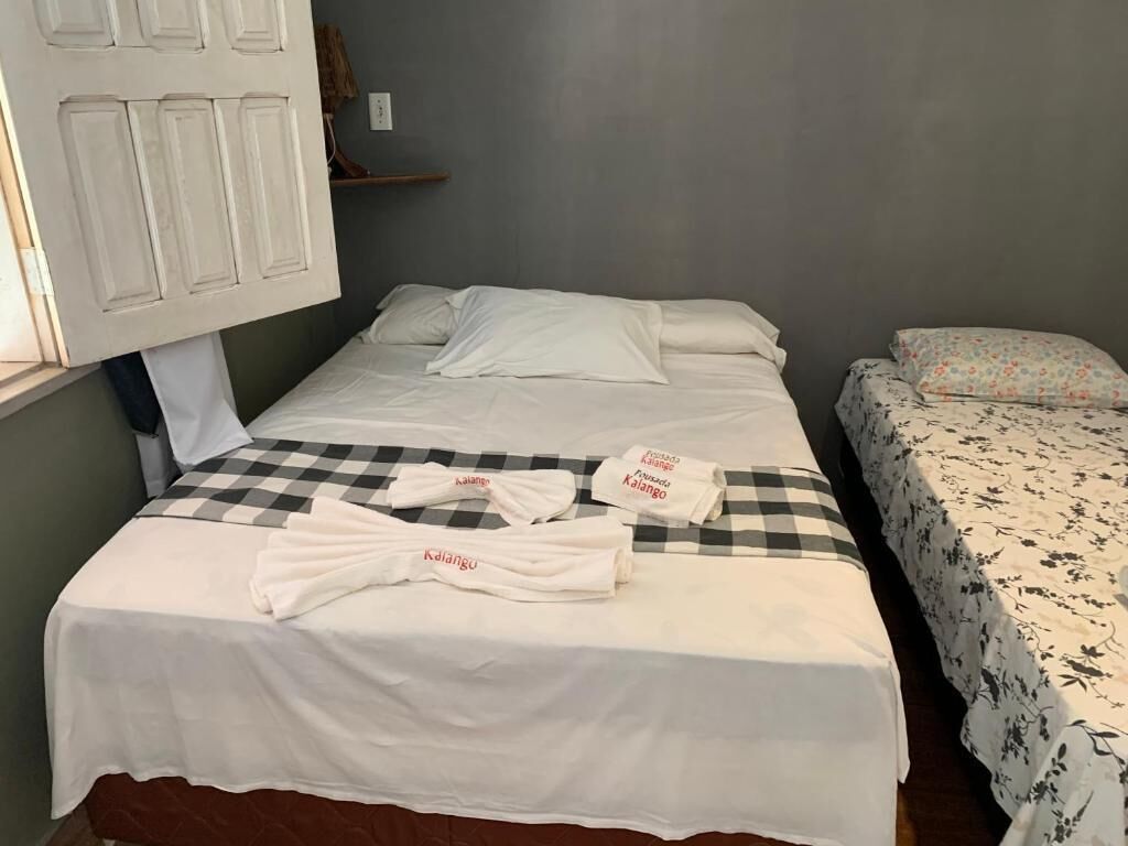 A room with two beds, one with a checkered bedspread and the other with a floral one. There are towels with text on them.