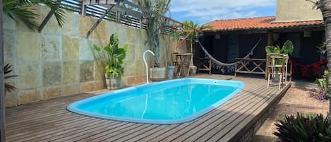 Una piscina rectangular con cubierta de madera, rodeada de muros de piedra y palmeras.