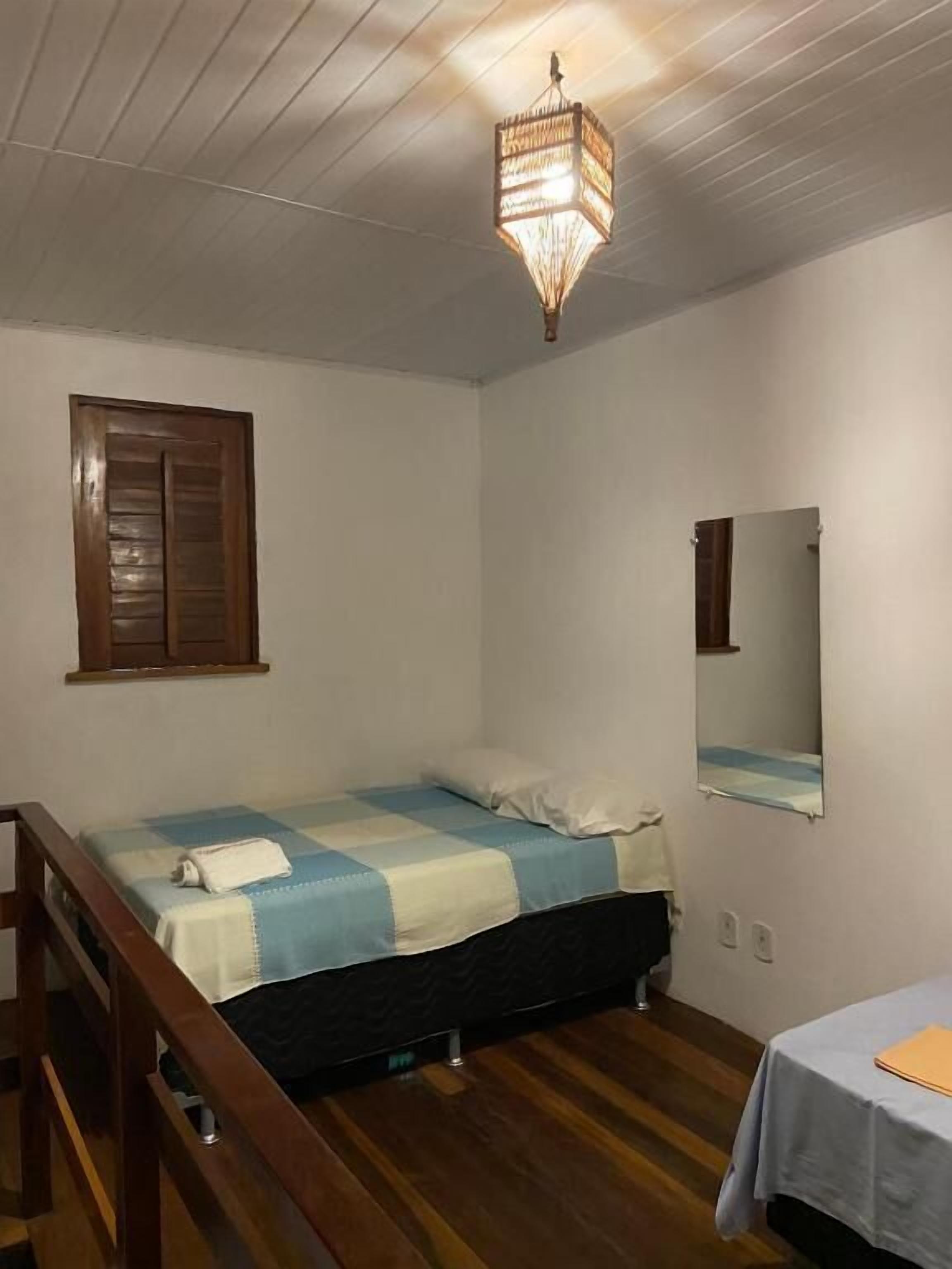 A bedroom with a bed, a wooden headboard, a bedside table, a mirror, and a hanging light fixture.
