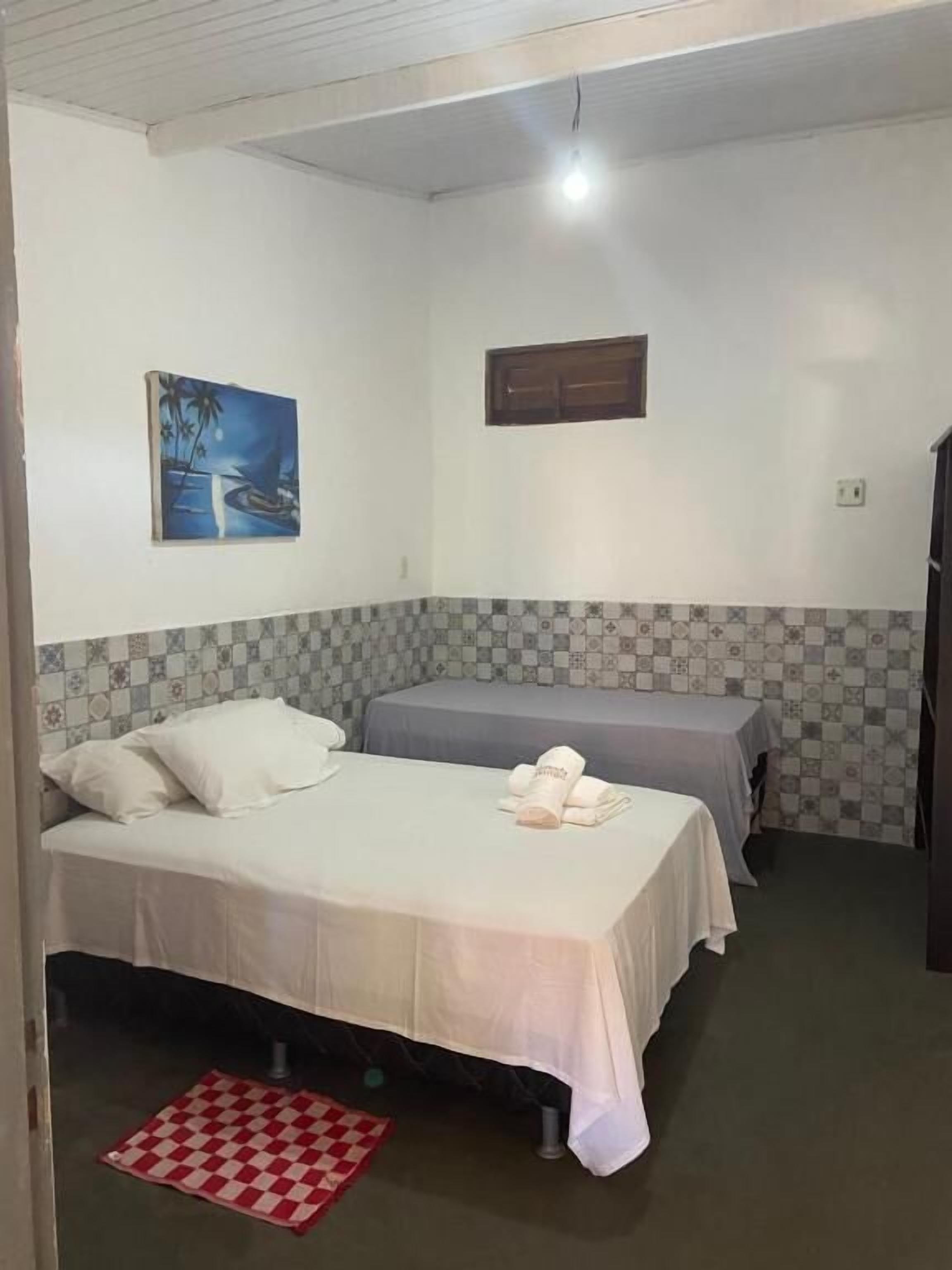 A room with two beds, a checkered rug, a painting, and a tiled wall.