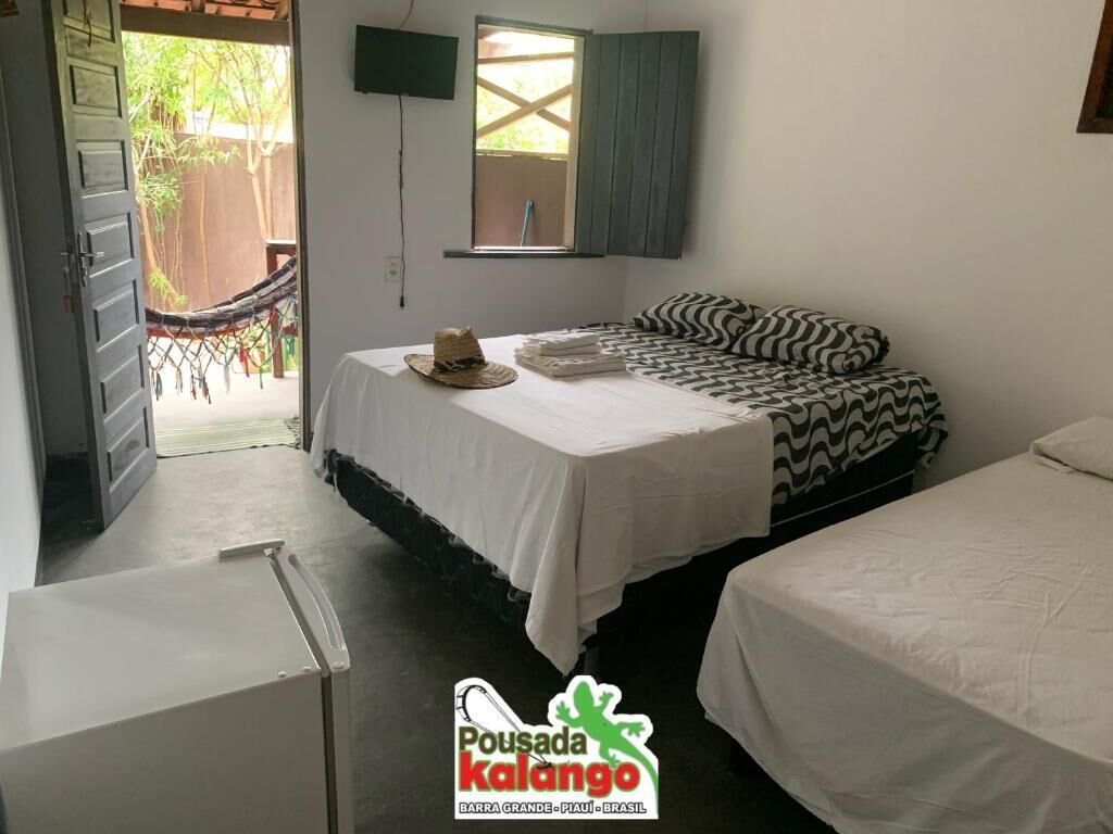 A bedroom with a bed, a small table, a window with shutters, and a view of a hammock outside.