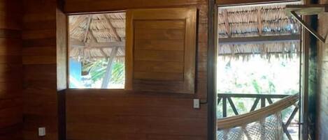 A wooden room with a bed, a hanging light fixture, a window, and a view of a blue pool.