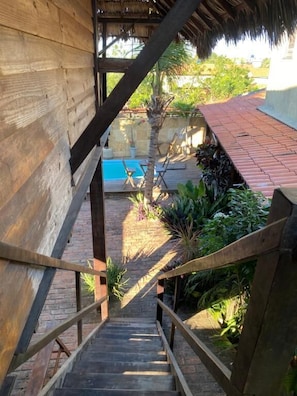A wooden staircase leading to a pool area with a thatched roof and outdoor seating. - Pousada Kalango (Cajueiro da Praia)