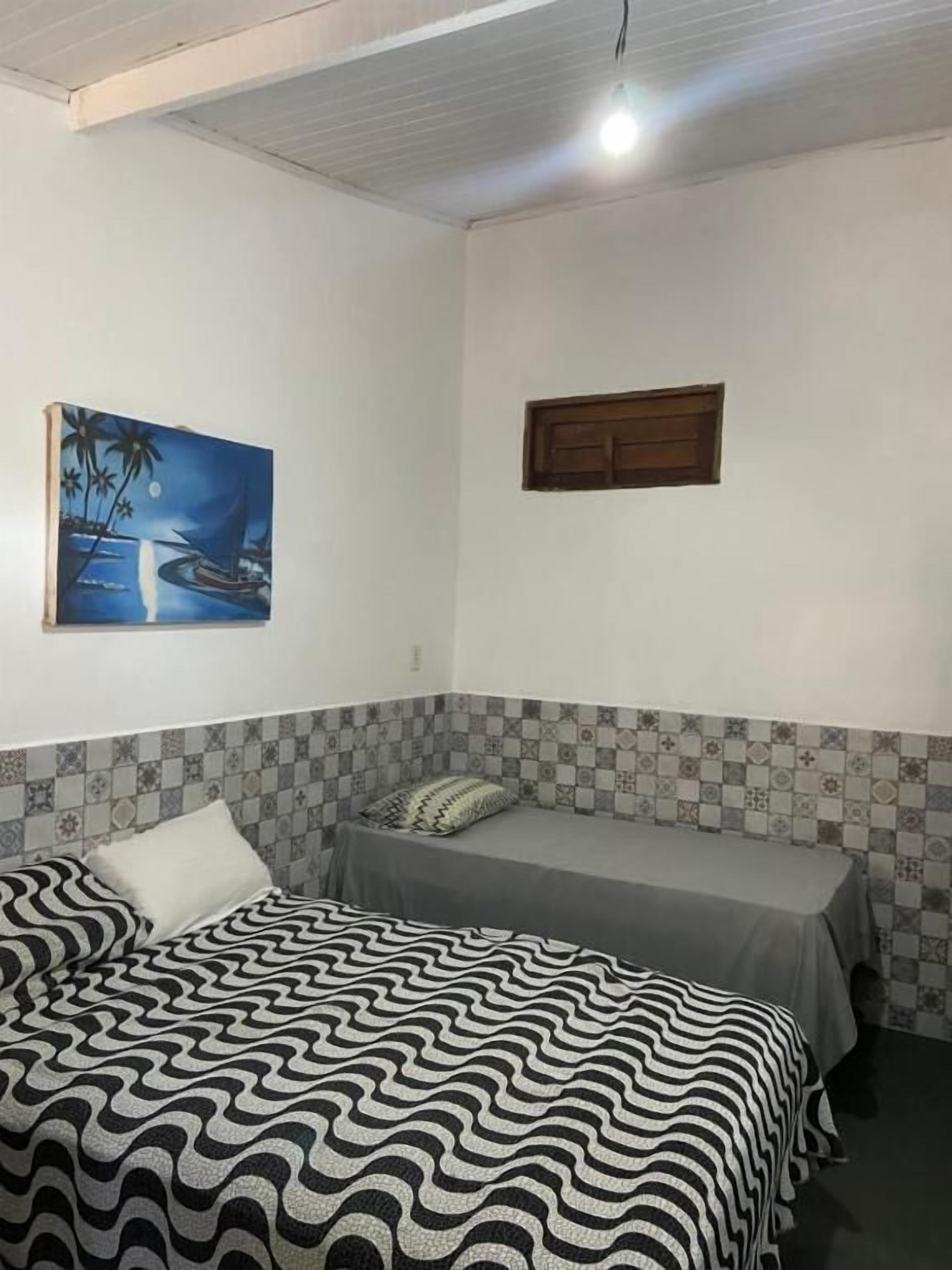 A room with a bed, a smaller bed, a painting, and a window.