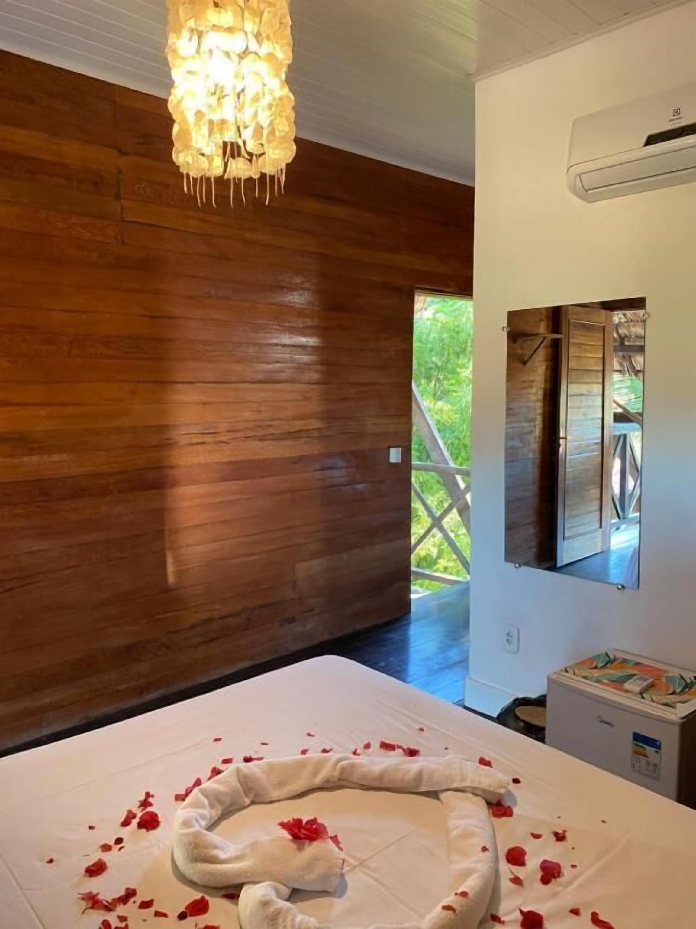 A room with wooden walls, a bed with rose petals, a chandelier, and a window with a view.