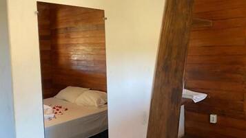Una habitación pequeña con cama, un refrigerador compacto, un espejo y aire acondicionado.