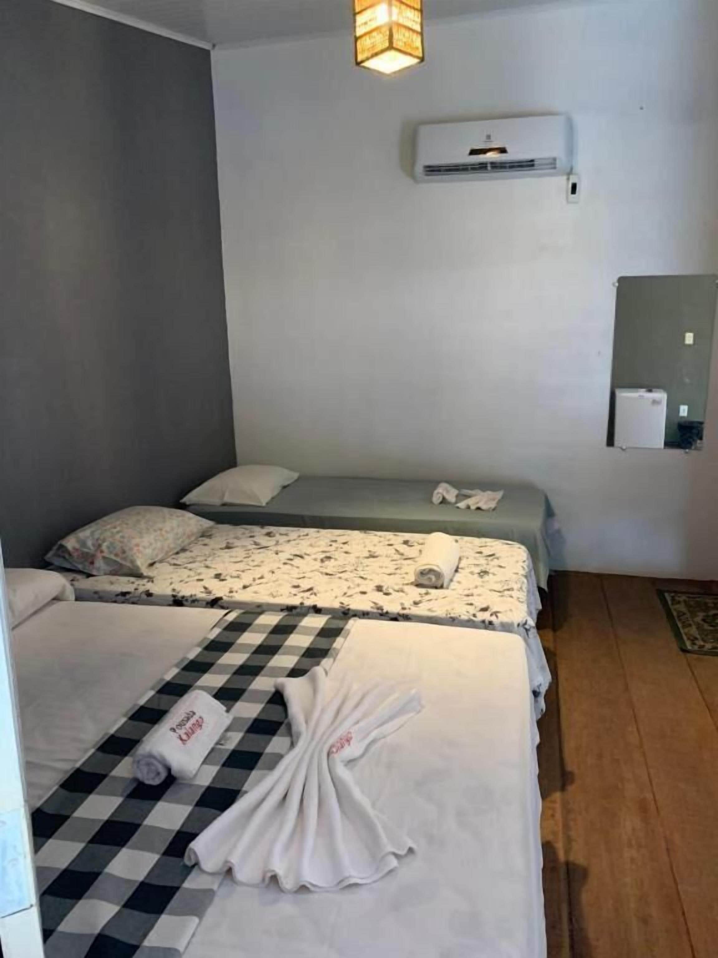 Habitación de hotel con dos camas, un corredor de cama a cuadros, una toalla, un equipo de aire acondicionado y una mesita con una lámpara.