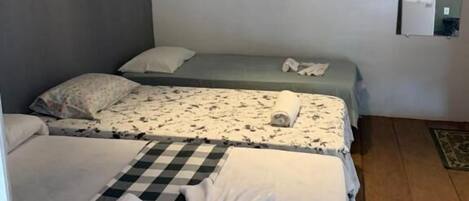 Habitación de hotel con dos camas, un corredor de cama a cuadros, una toalla, un equipo de aire acondicionado y una mesita con una lámpara.