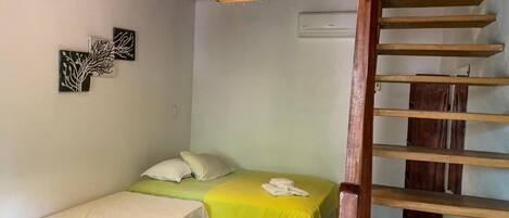 Una habitación con dos camas, una lámpara colgante, un equipo de aire acondicionado y una escalera de madera.