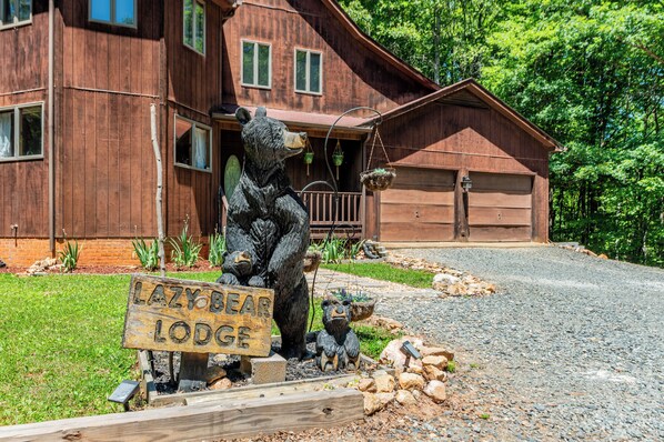 A wooden cabin with a bear statue, a sign reading 'Lazy Bear Lodge,' and a gravel driveway.