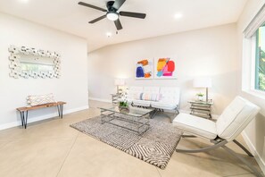 Un salon moderne avec une table basse en verre, un canapé, un banc, un tapis à motifs et des œuvres d’art abstraites accrochées au mur.