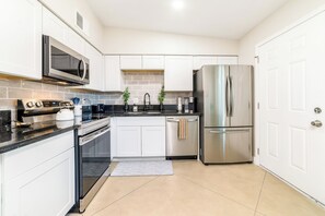 Una cocina moderna con armarios blancos, electrodomésticos de acero inoxidable y salpicadero de azulejos.