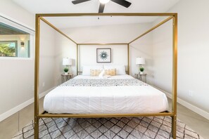 Un letto a baldacchino con copripiumino bianco, due lampade ai lati del letto, una decorazione a forma di stella appesa al muro e vista su del verde all'esterno.