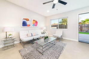 Un salon spacieux avec un canapé blanc, une table basse en verre et un ventilateur de plafond.