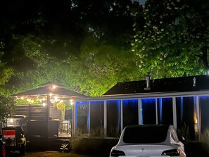 Ein Gebäude mit überdachter Außenfläche, einem davor geparkten Auto und einem Baum im Hintergrund.