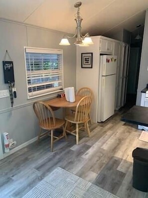 Eine kleine Küche mit Esstisch, Stühlen, einem Kühlschrank und einem Fenster mit Jalousien.
