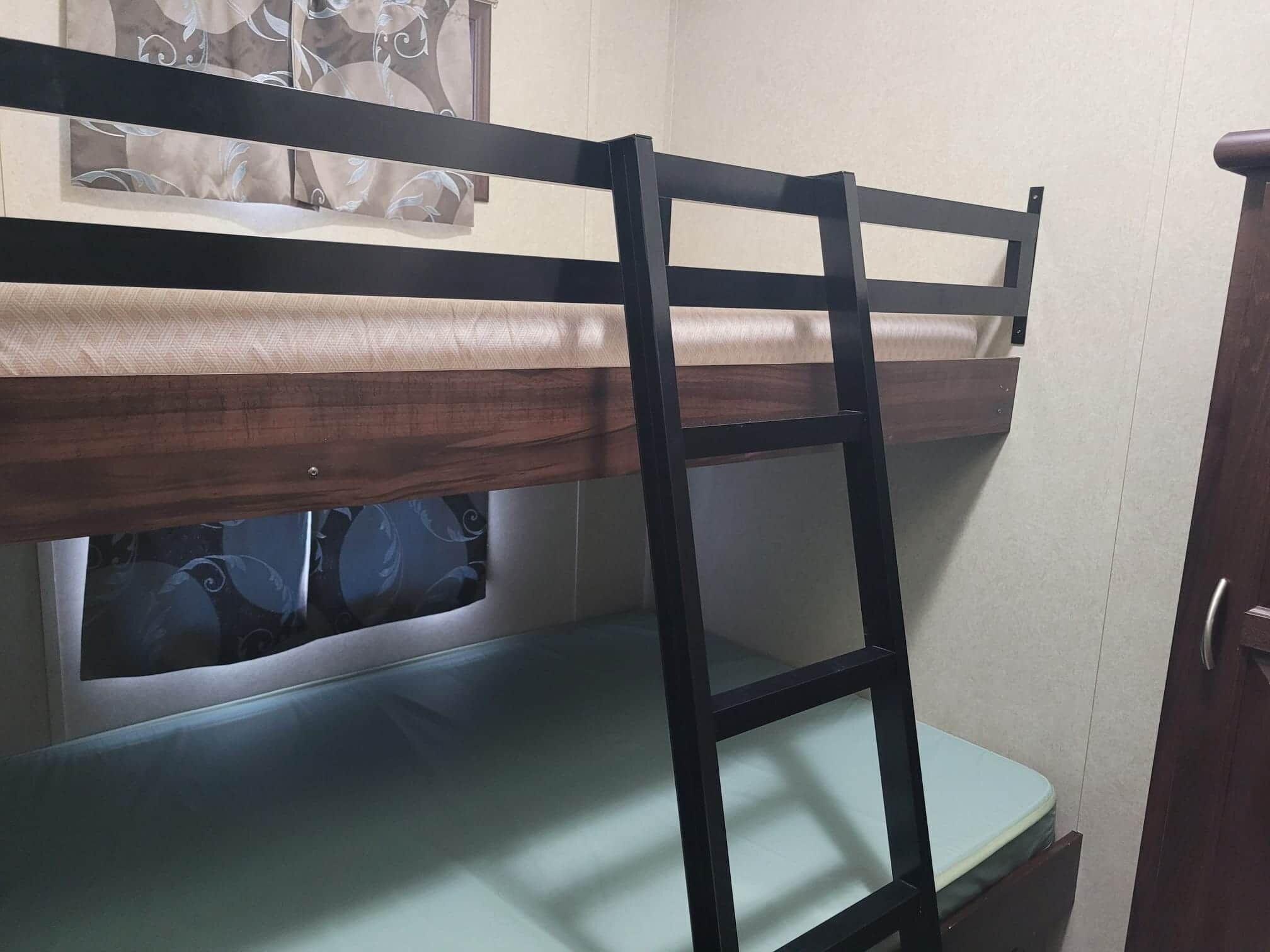Un lit superposé avec une échelle, une fenêtre avec des rideaux et une porte.
