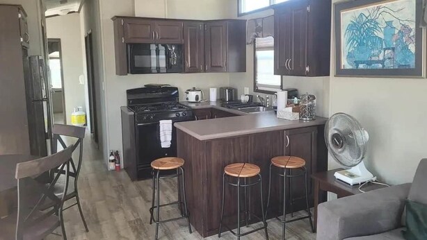 Una cocina con armarios de madera oscura, una isla central con taburetes, un microondas, estufa y un ventilador.