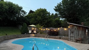 A swimming pool with a wooden deck, a small shed, and a fence with string lights. - 4BR Home - Airport- UD - WPAFB - POOL -Sleeps 7 (Dayton)