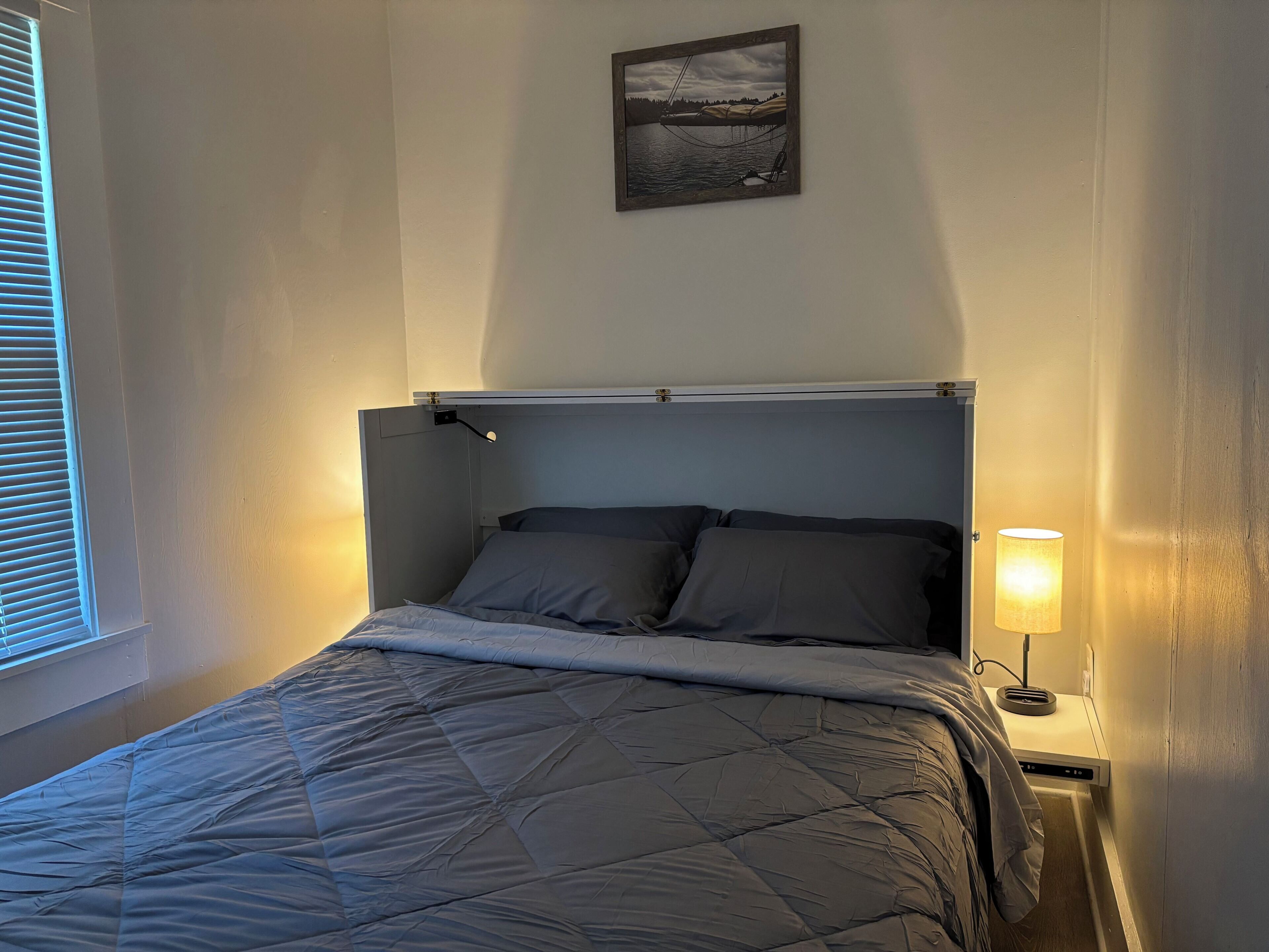 Una cama con cubrecolcha acolchado, una lámpara de noche y un cuadro enmarcado en la pared.