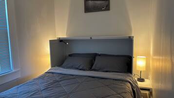 Una cama con cubrecolcha acolchado, una lámpara de noche y un cuadro enmarcado en la pared.