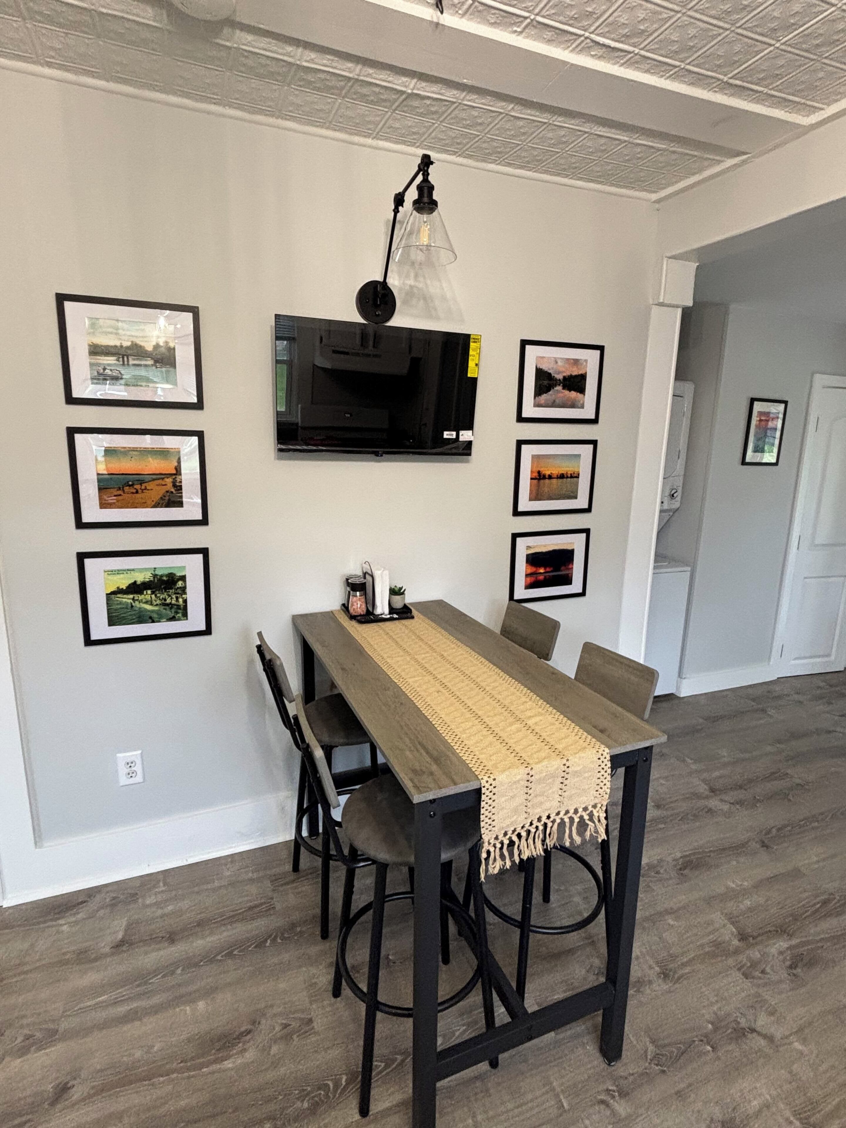 A dining area with a table, chairs, a hanging light fixture, and framed pictures on the wall.