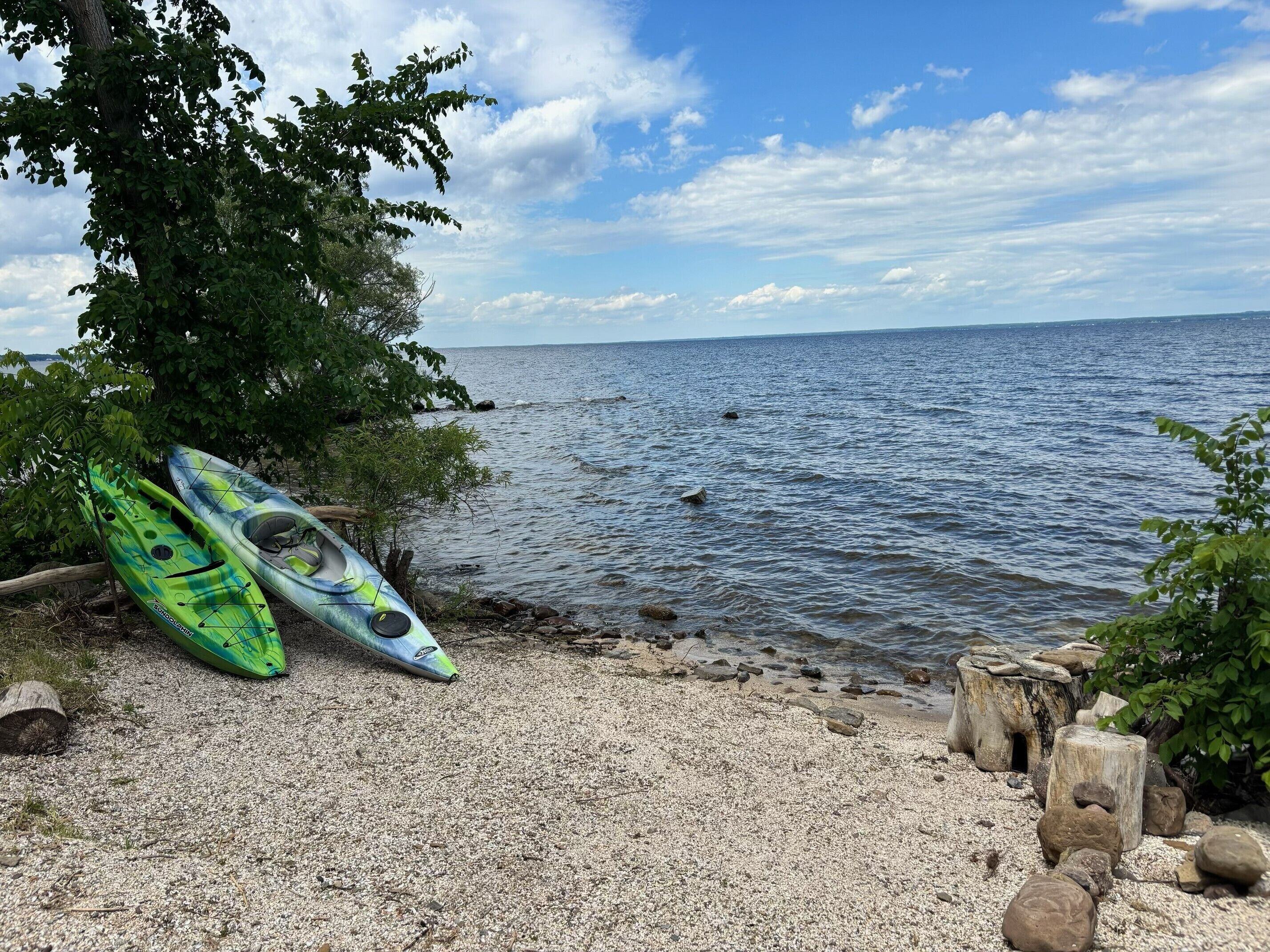 A pebbled beach with kayaks and a wooden stump.