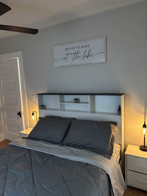 A bedroom with a bed, bedside tables, a wall-mounted shelf, and a sign above the bed.