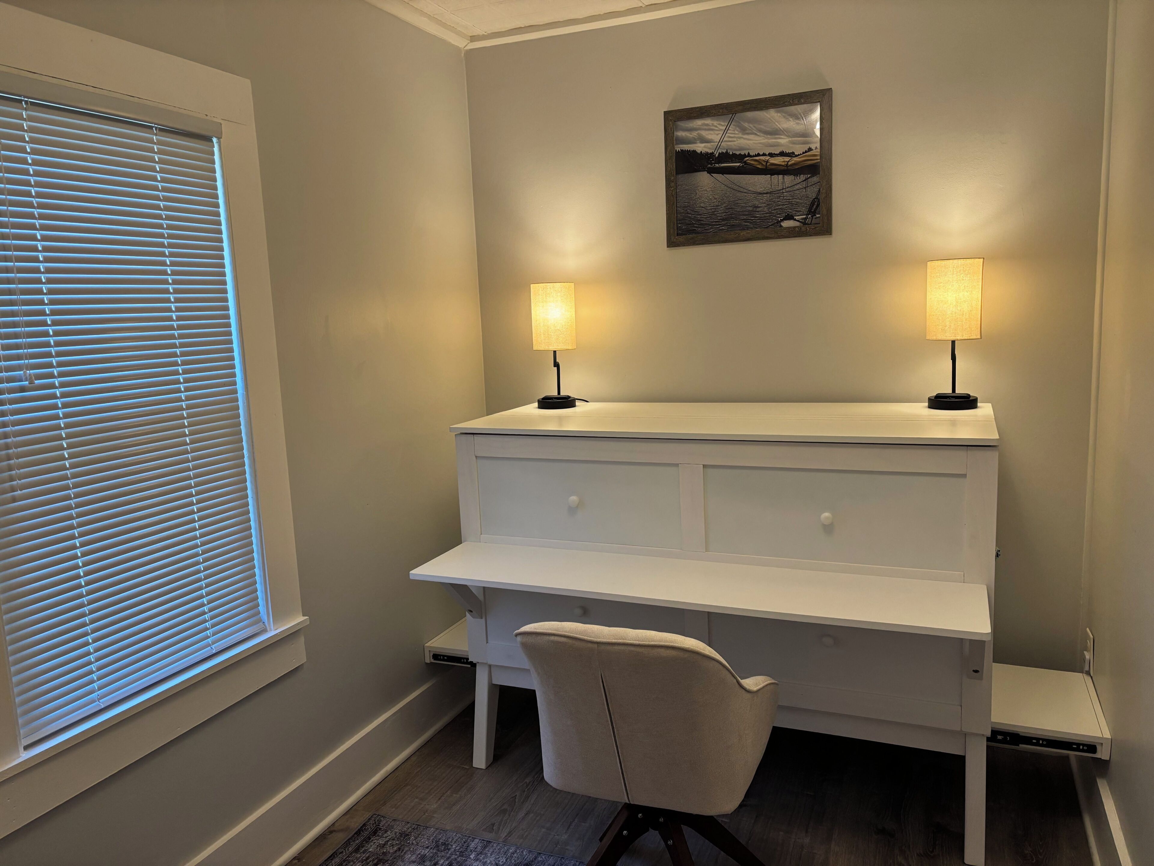 Une pièce comprenant un bureau, deux lampes, une chaise et un tableau encadré accroché au mur.