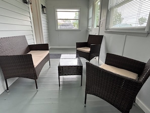 A covered patio with wicker furniture, a glass table, and a view of the outside.