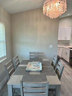 A dining area with a table, chairs, a decorative light fixture, and a kitchen in the background. - Beautiful home near Warm Springs (North Port)