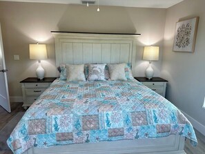 A bedroom with a bed, two bedside tables, two lamps, a nightstand, a wall-mounted artwork, and a door. - Beautiful home near Warm Springs (North Port)