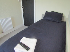 A bed with a dark blanket, a pillow, and a remote control on a white pillow. - No 12 GuestHouse (Blackpool)