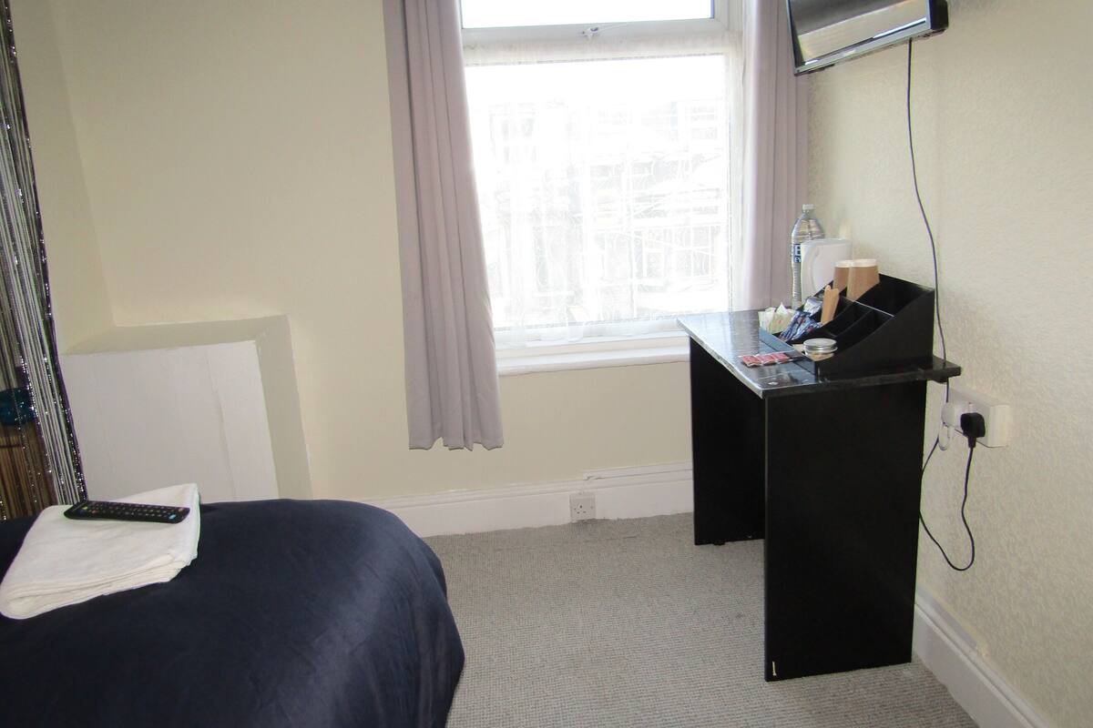 A hotel room with a bed, a desk, a window, and a television.