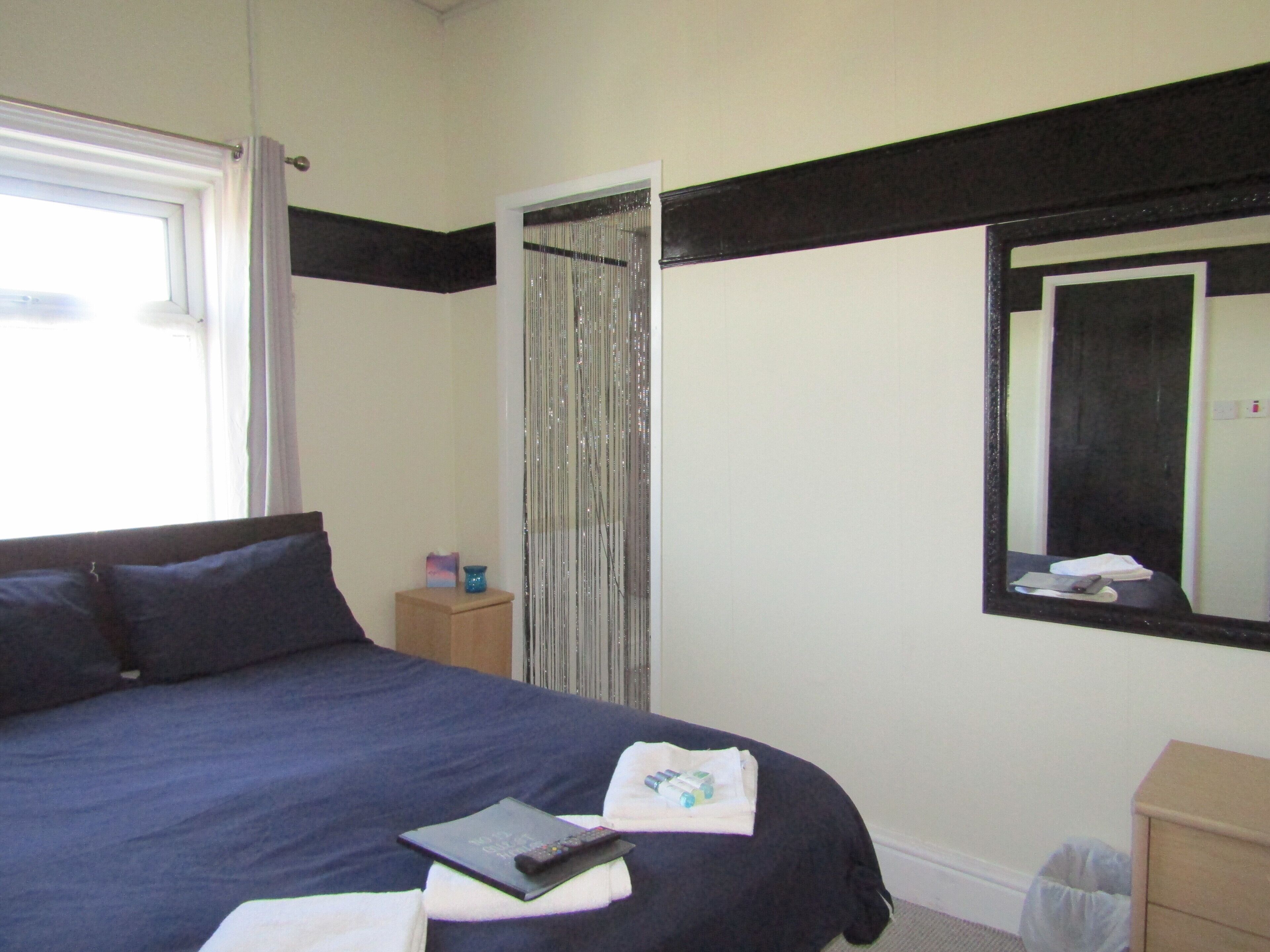 A bedroom with a bed, a bedside table, a mirror, and a window.