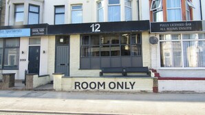 Um edifício com um letreiro indicando 'ROOM ONLY', um letreiro de 'BAR TOTALMENTE LEGALIZADO' e um letreiro de 'RESERVAR AGORA'.