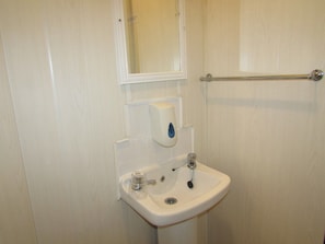 Een badkamer met een wit wastafel, een spiegel en een zeepdispenser.