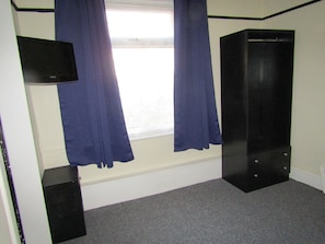 Een kamer met een raam, blauwe gordijnen, een zwarte kast en een flatscreen televisie aan de muur.