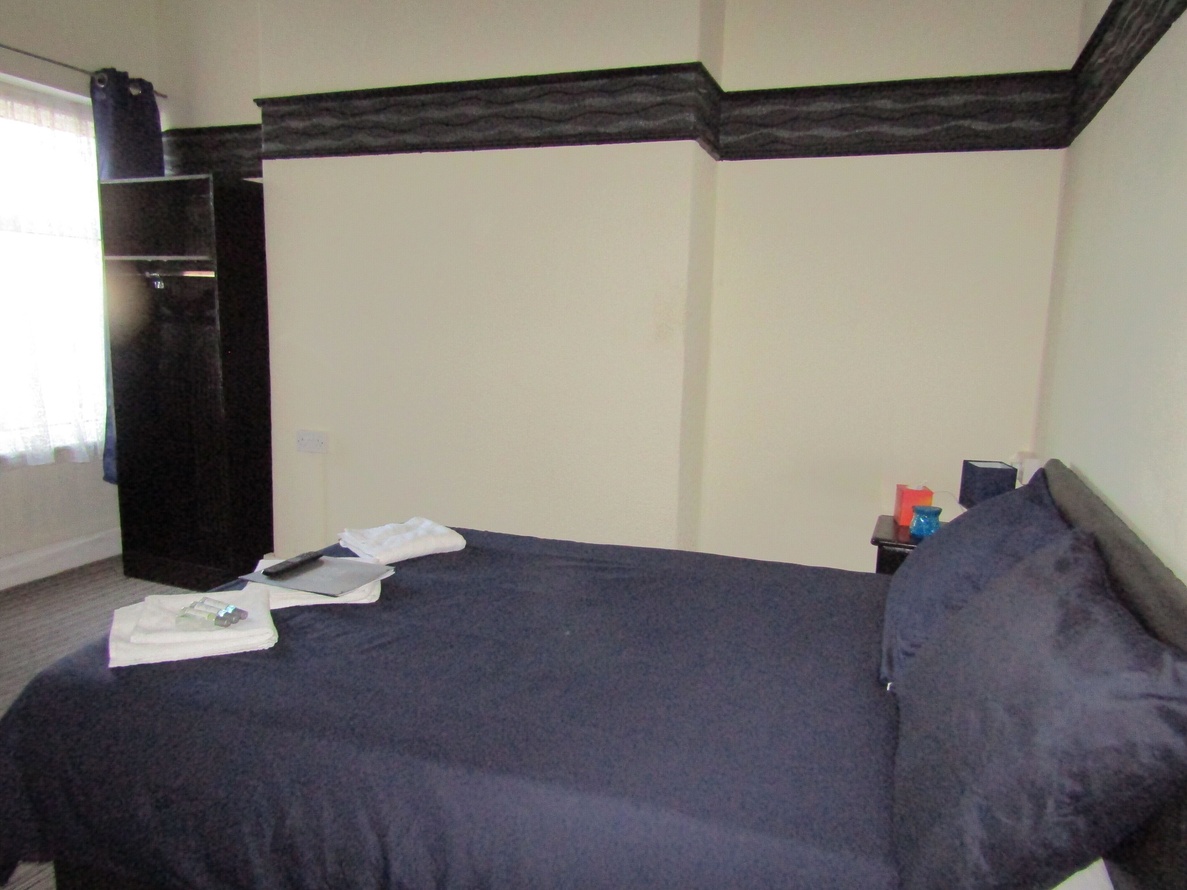 A bedroom with a bed, a nightstand, a dresser, and a window with curtains.
