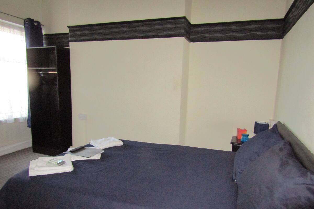 A bedroom with a bed, a nightstand, a dresser, and a window with curtains.