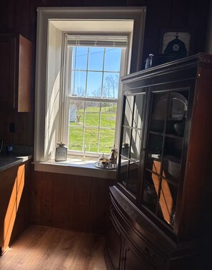A kitchen with a window, wooden cabinets, a cabinet with glass doors, and a view of the outdoors. - 3-bedroom farmhouse in tranquil Bedford with cozy charm (Bedford)