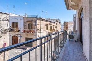 Un balcone con ringhiera in metallo che si affaccia su una strada con edifici, un segnale di divieto di sosta e un armadio elettrico.