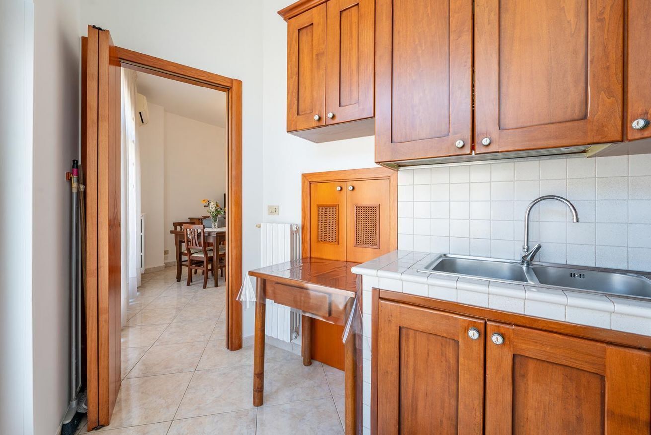 Cozinha com armários de madeira, pia e área de refeições com cadeiras e mesa.