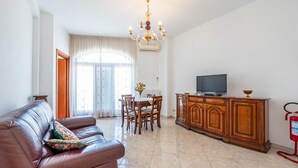 A living room with a leather sofa, a dining table with chairs, a wooden cabinet, a television, and a chandelier. - Nacci White Home by Rentbeat (Ostuni)