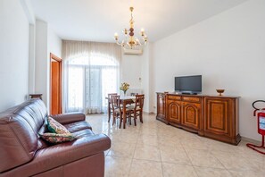 Un soggiorno con un divano in pelle, un tavolo da pranzo con sedie, un mobiletto in legno, una televisione e un lampadario.